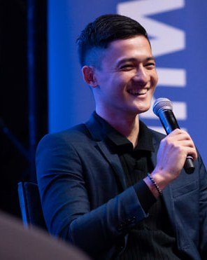 Kyle tersenyum sambil memegang mikrofon di atas pentas